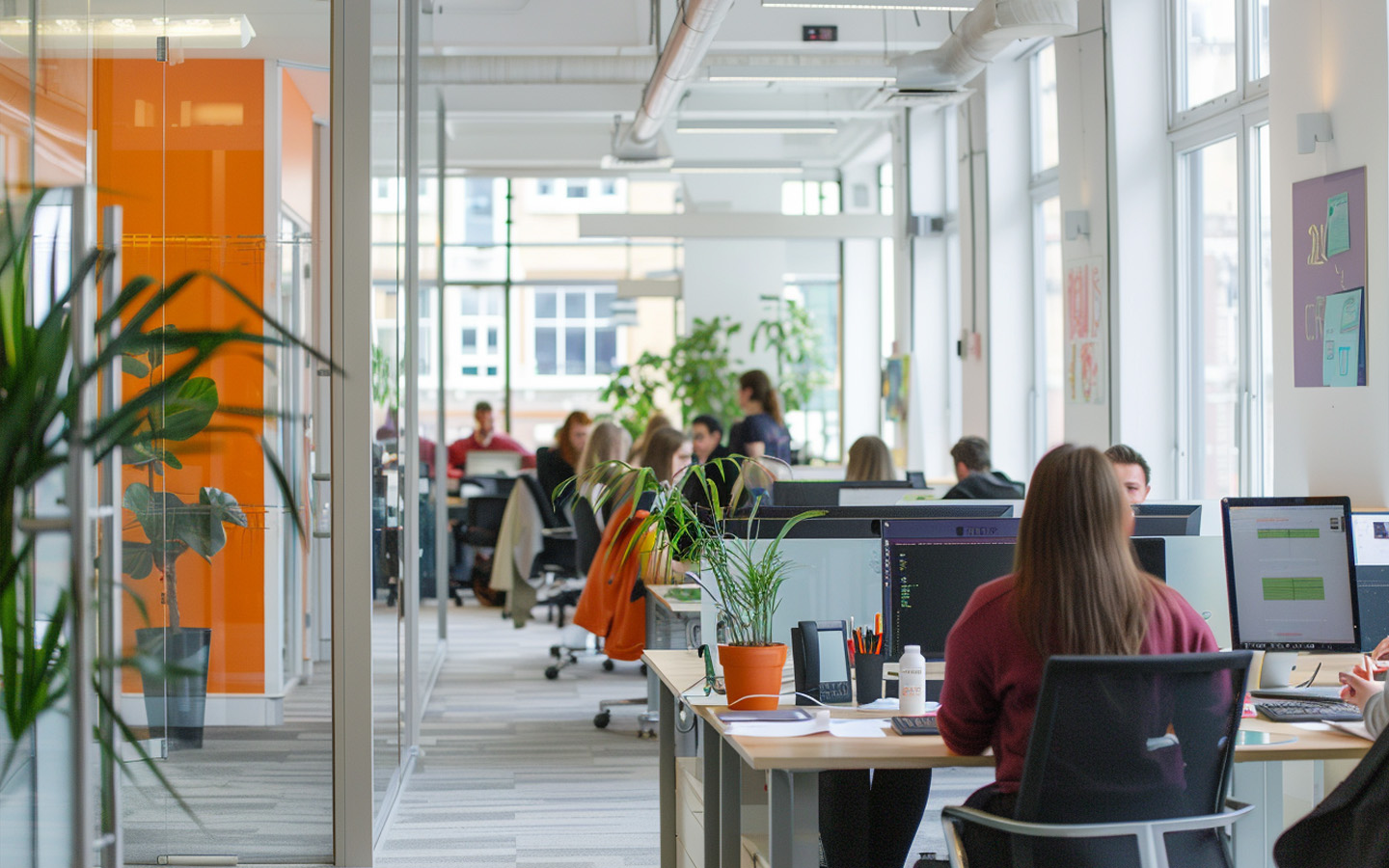 Modern office space with employees working at desks, featuring glass partitions and potted plants
